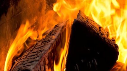 Blick in ein Kaminfeuer mit Betonung auf die weich züngelnden Flammen und die Gluthitze unter dem Kaminholz